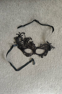 Antifaz bordado negro con cinta para atar, la pieza sobre fondo gris. Ker Lingerie